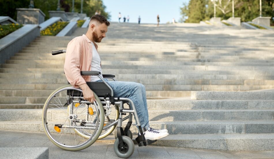 Een man in een rolstoel bij een trap die niet rolstoeltoegankelijk is